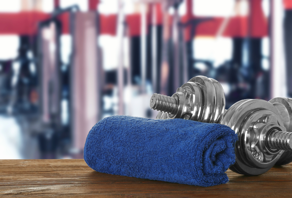 Towel,And,Dumbbells,On,Table,Against,Blurred,Gym,Interior,Background